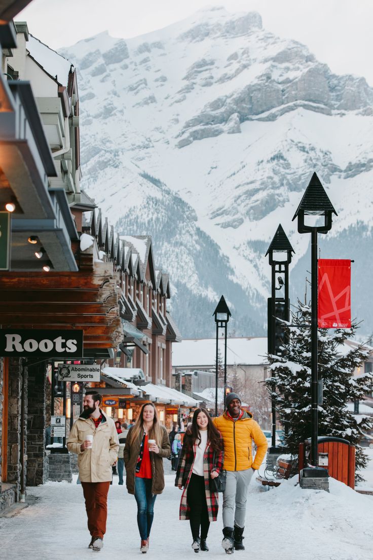 several people walking down a snowy street in front of buildings with mountains in the background