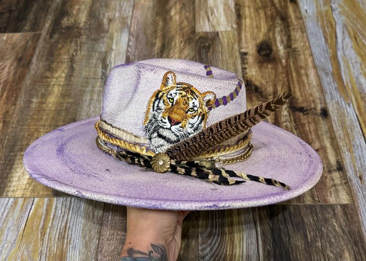 ✨THIS IS A CUSTOM HAT BAND ONLY✨ Made to fit most hats with a tie closure.  One of a kind purple and gold band with gold metallic tipped feather & unique pin to cheer on our Tigers in one of a kind style!!  ⭐️Please Note: Creating your order may take 10 to 14 days from the time your order is placed before it ships. ⭐️ Photos are examples that have been previously made. These are made to order. All bands, buttons, overall distressed look may vary slightly, since these are all one-of-a-kind pieces Adjustable Gold Fedora For Festivals, Adjustable Gold Fedora For Kentucky Derby, Purple Hat As A Gift, Purple Hats As Gifts, Adjustable Purple Top Hat With Curved Brim, Adjustable Gold Hat Band For Kentucky Derby, Adjustable Wide Brim Top Hat As Gift, Adjustable Wide Brim Gold Top Hat, Gold Top Hat With Adjustable Curved Brim