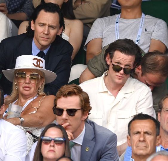 a man and woman sitting next to each other at a tennis match wearing sun glasses