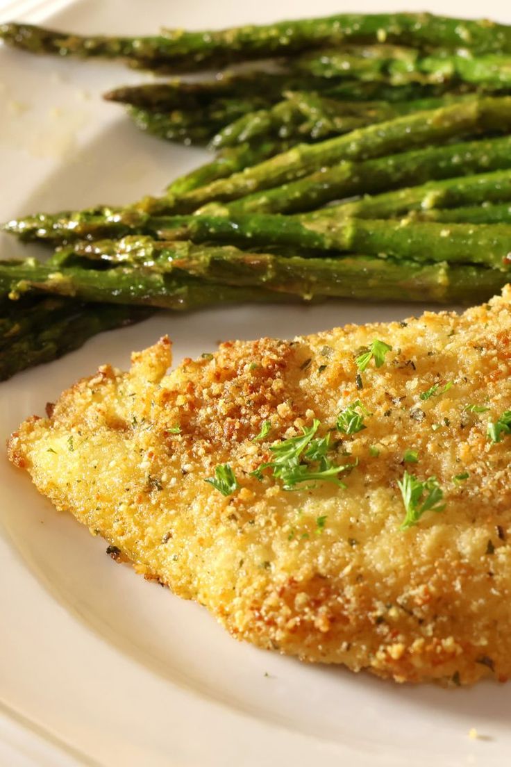 a white plate topped with asparagus and fried fish next to some breaded crumbs