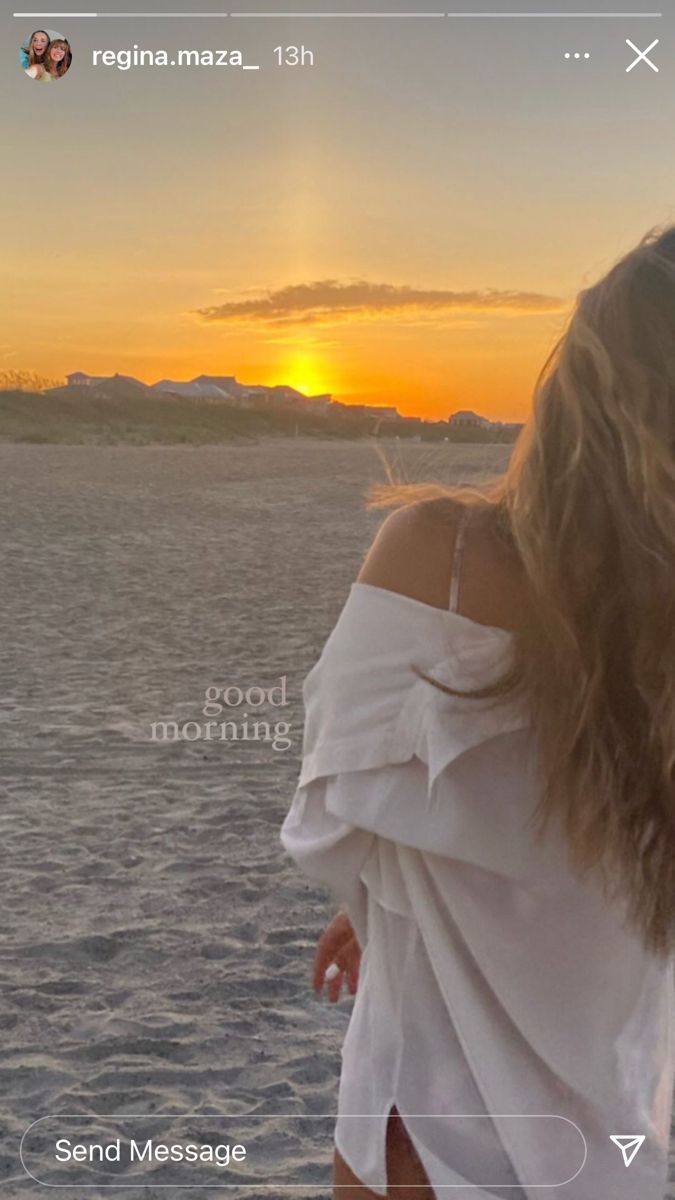 a woman standing on top of a sandy beach next to the ocean at sunset with her hair blowing in the wind