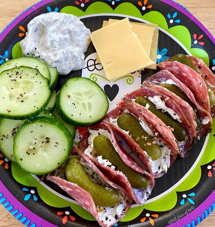 a plate with cucumbers, cheese and meat on it