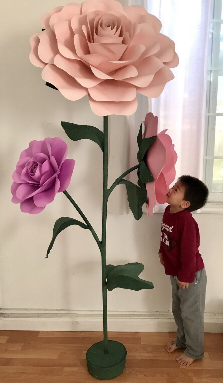 a young boy standing in front of a paper flower sculpture that looks like a giant rose