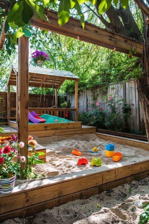 an outdoor play area with sand and toys in the middle, surrounded by flowers and trees