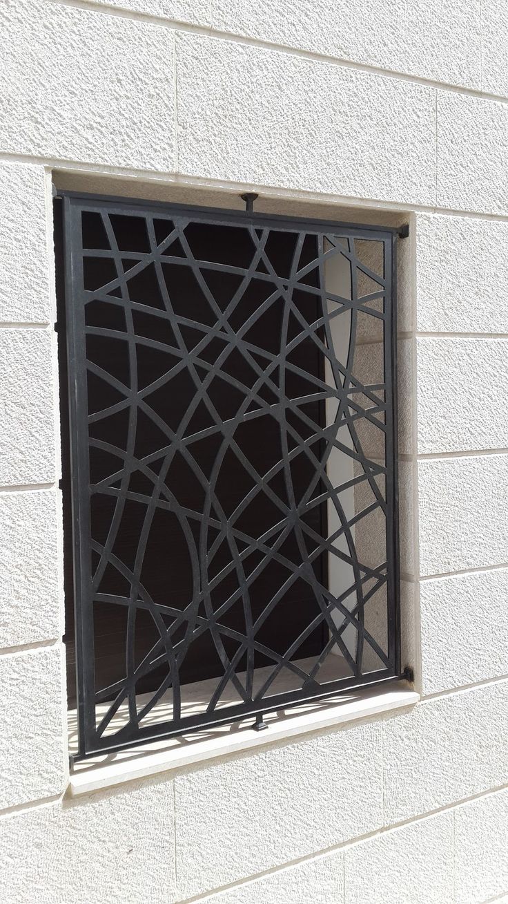 a window that is on the side of a white brick building with black iron bars