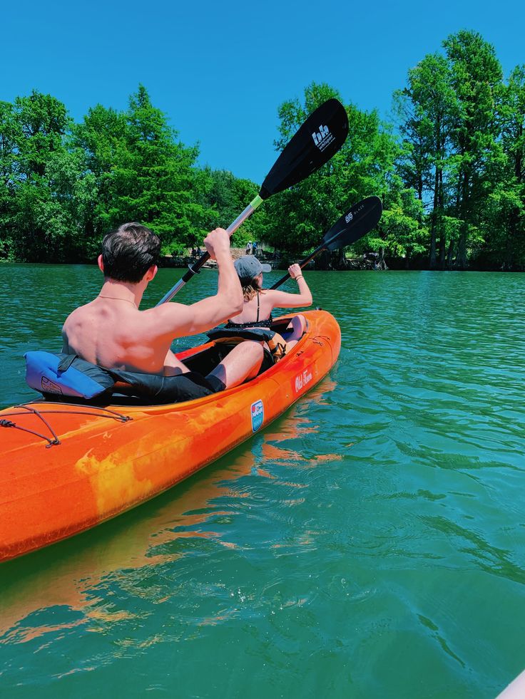 a man in an orange kayak paddles through the water on a sunny day