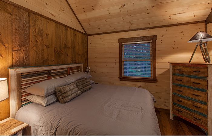 a bed in a bedroom next to a lamp and window with wood paneling on the walls