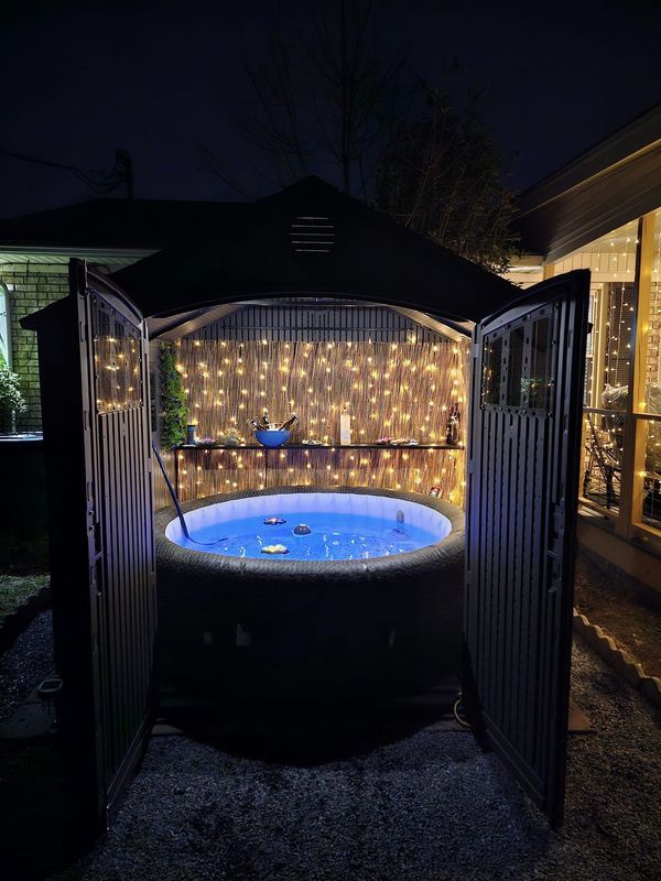 an outdoor hot tub is lit up with fairy lights and surrounded by a fenced in area