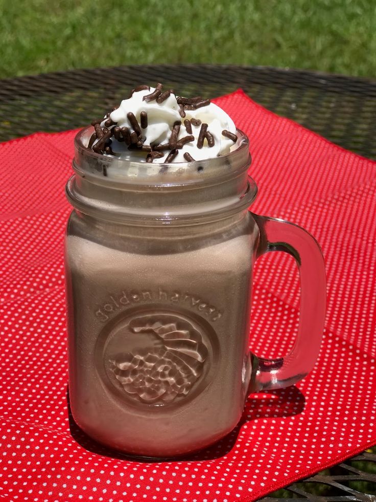 a mason jar filled with whipped cream and chocolate sprinkles on a red tablecloth