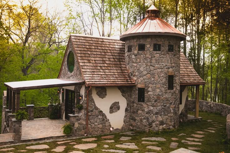 a stone house with a copper roof in the middle of some trees and stones on the ground