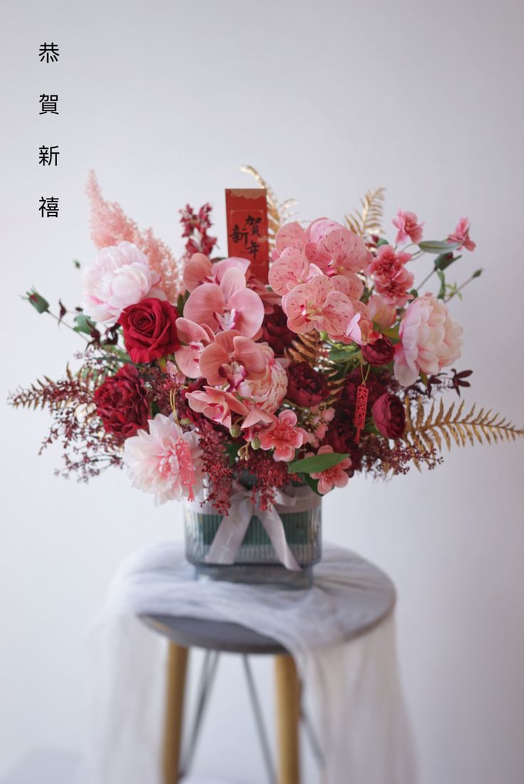 an arrangement of flowers in a vase on a small stool with chinese characters above it