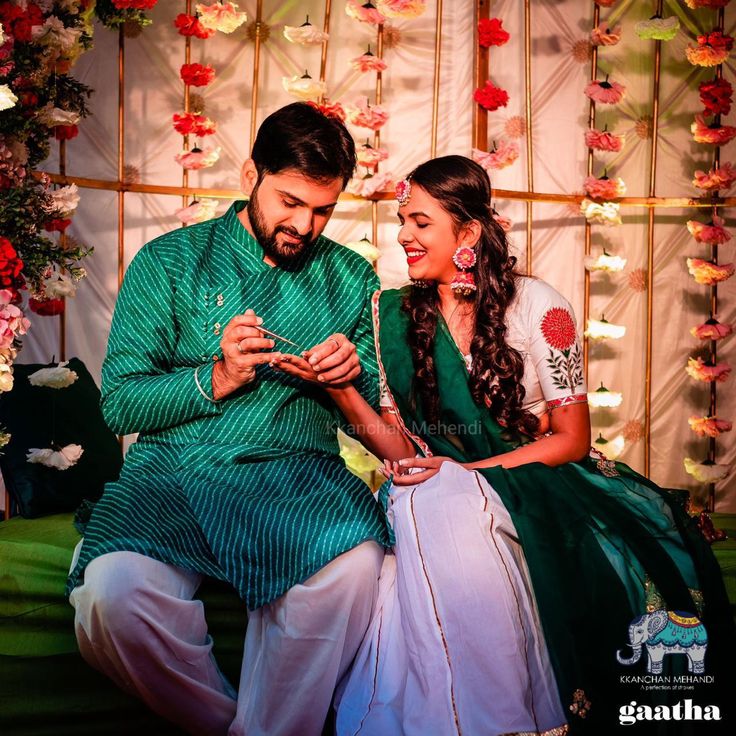 a man and woman sitting next to each other in front of a wall with flowers