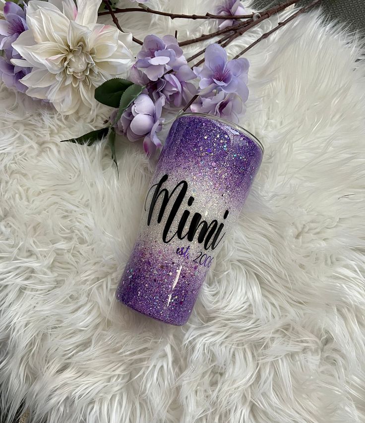 a purple glitter tumbler with the word mimi on it next to some white flowers