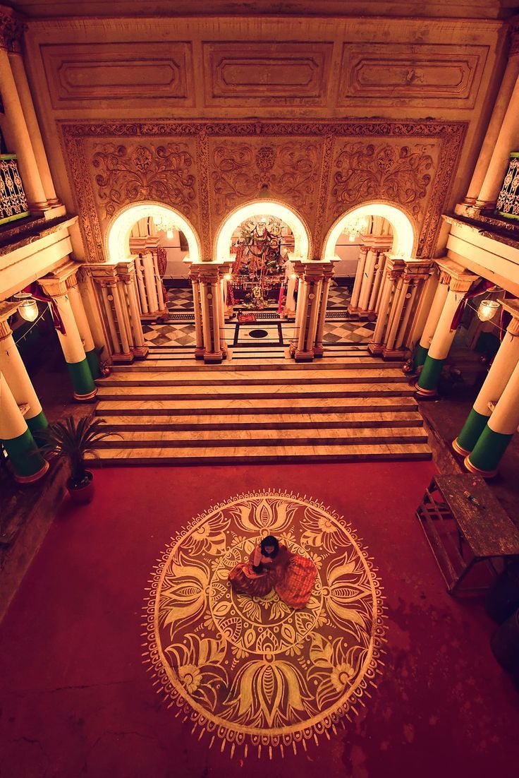 a woman sitting on top of a red rug in a room with columns and arches