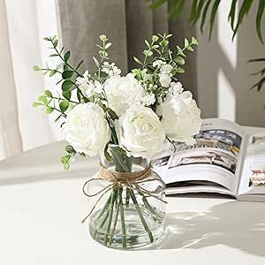 a vase filled with white flowers on top of a table next to an open book