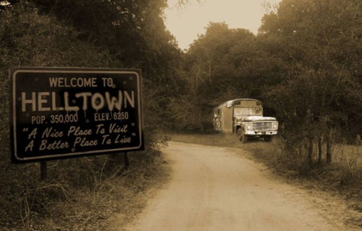 an old truck driving down a dirt road next to a sign that says hell town