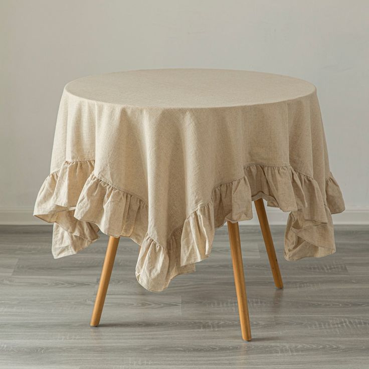 a round table with ruffles on it in front of a white wall and wood floor