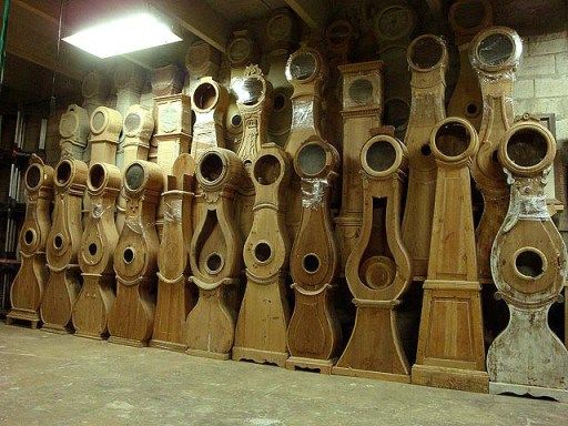 a large group of wooden clocks sitting on top of each other in a room next to a brick wall