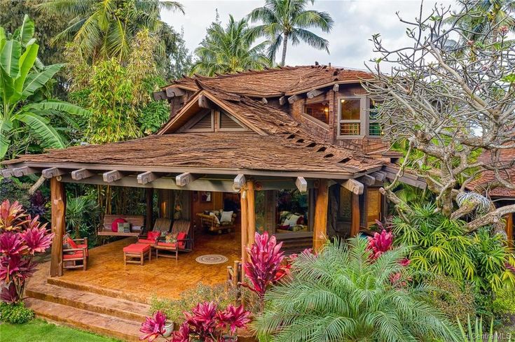 a wooden house surrounded by lush green trees and flowers in the foreground is an outdoor patio with seating area