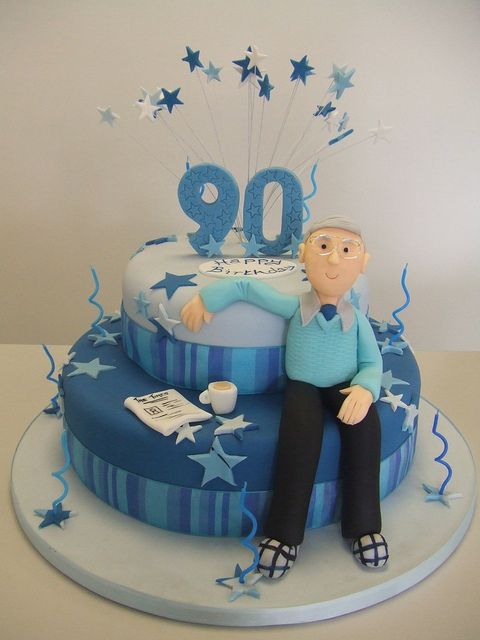 a birthday cake with a man sitting on top of it and blue stars around the base