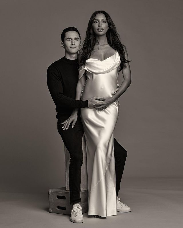 a man standing next to a woman in a white dress and black pants, posing for the camera