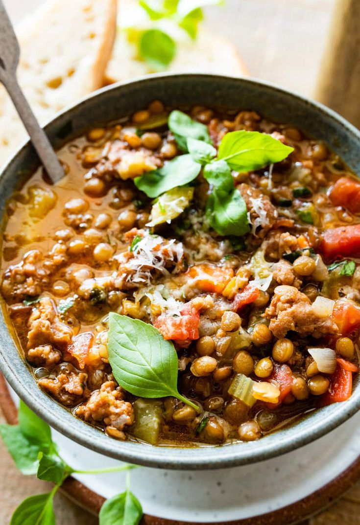 a bowl filled with beans and vegetables on top of a wooden table next to bread