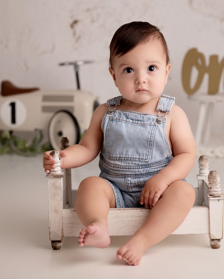 a baby is sitting on a small wooden bench with his legs crossed and looking at the camera