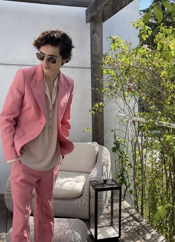 a man in a pink suit and sunglasses standing on a porch next to a white couch