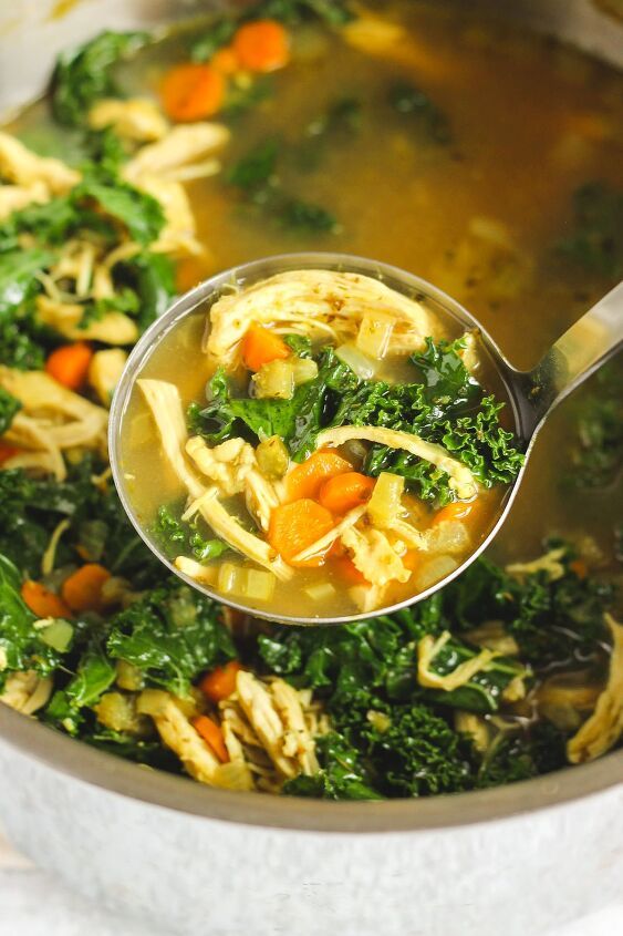 a ladle full of chicken noodle soup with carrots and spinach