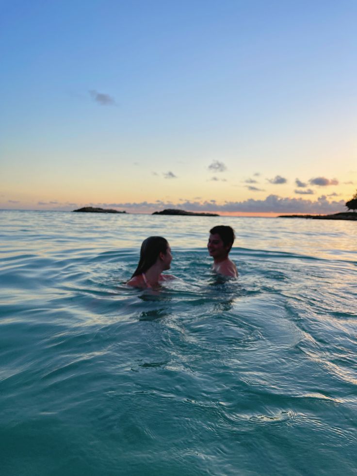 two people are swimming in the ocean at sunset or sunrise, one is holding his head back