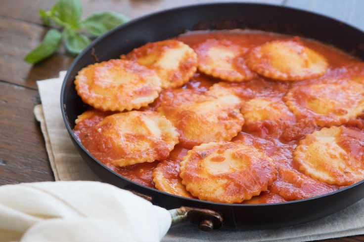 a pan filled with ravioli and sauce on top of a wooden table next to a napkin