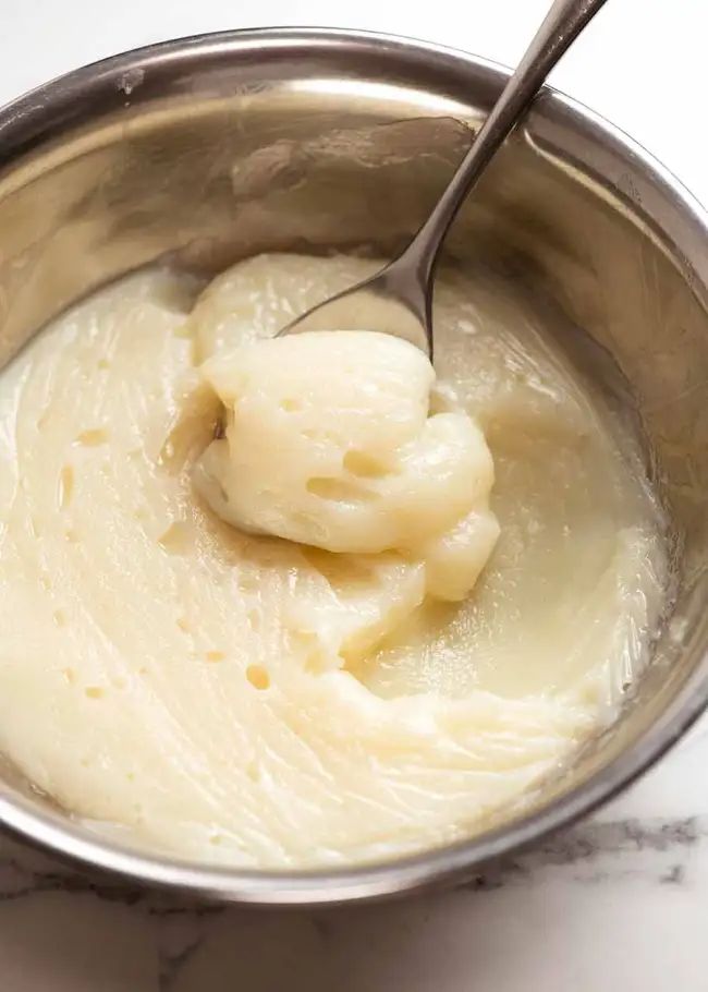 a metal bowl filled with cream on top of a white marble countertop next to a silver spoon