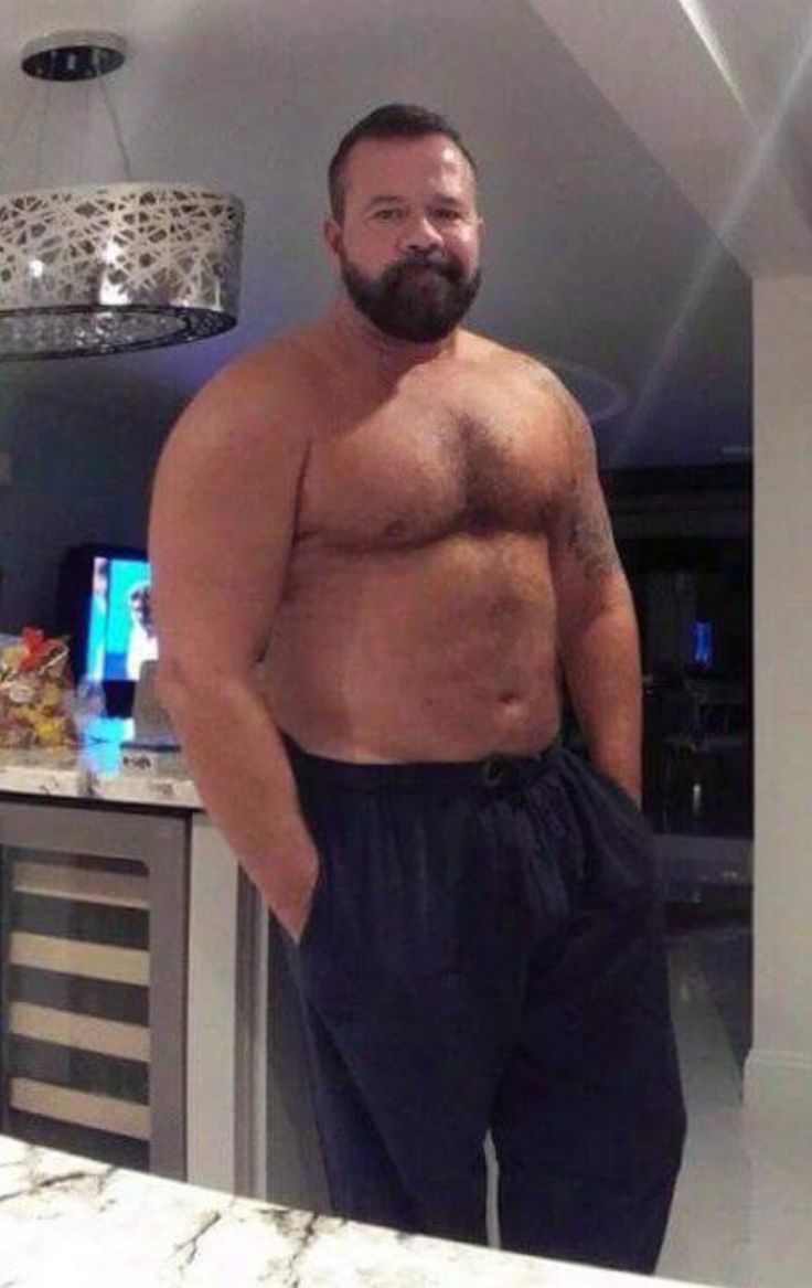 a man with no shirt standing in front of a kitchen counter and looking at the camera