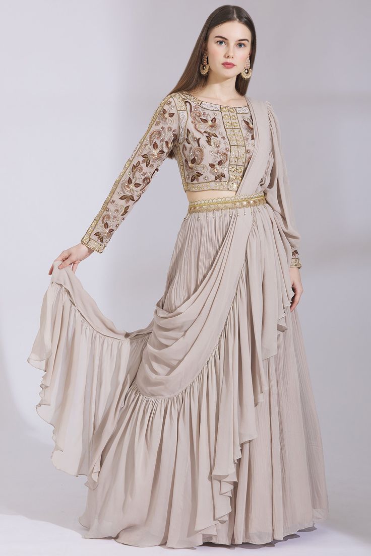 Taupe lehenga with attached drape and ruffle border. Comes with floral motif worked blouse.
Components: 2
Fabric: Georgette
Neckline: Round
Sleeve Length: Full
Color: Grey
Embroidered
Draped lehenga
Gathered flare
Ruffle detail
Closure: Blouse: Back zip
Note: Belt worn by the model is not for sale
 - Aza Fashions Festive Floor-length Georgette Skirt Set, Elegant Floor-length Skirt Set With Dupatta, Draped Georgette Designer Lehenga, Semi-stitched Georgette Skirt Set For Reception, Draped Georgette Lehenga For Reception, Elegant Skirt Set With Zari Work In Traditional Drape, Designer Wear Floor-length Skirt Set With Resham Embroidery, Designer Floor-length Skirt Set With Resham Embroidery, Anarkali Style Dupatta With Ruffles In Traditional Drape