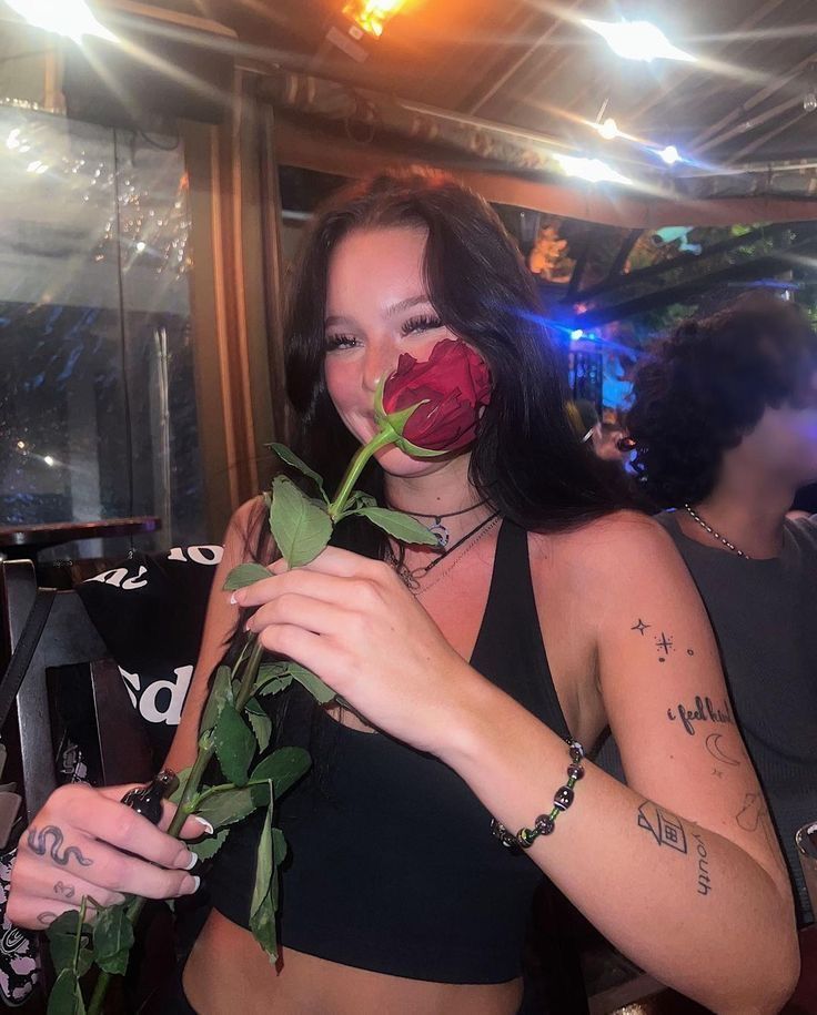 a woman holding a rose in her right hand and wearing tattoos on her left arm