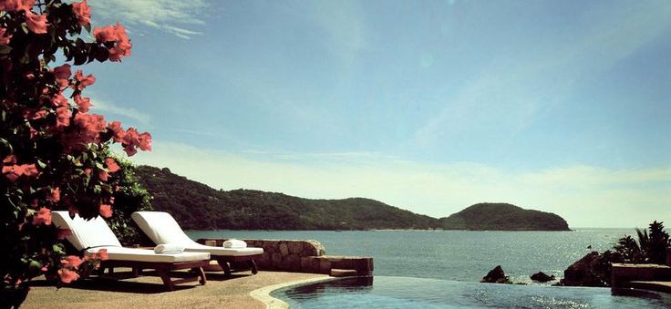 two chaise lounge chairs sitting next to an outdoor swimming pool overlooking the ocean and mountains