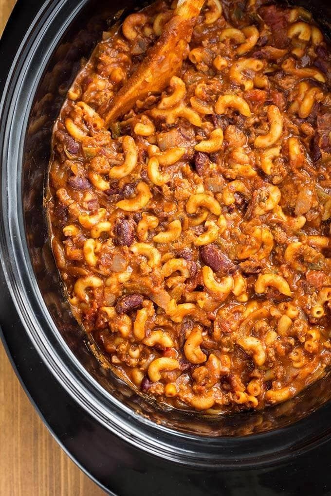 a crock pot filled with macaroni and cheese on top of a wooden table