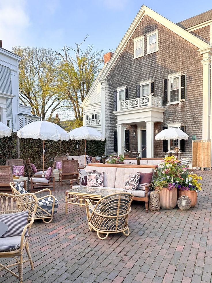 an outdoor seating area with umbrellas, chairs and potted plants in front of a house