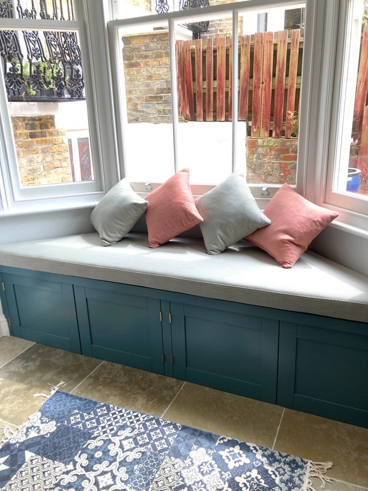 a window seat with three pillows on it in front of a brick wall and blue cabinetry