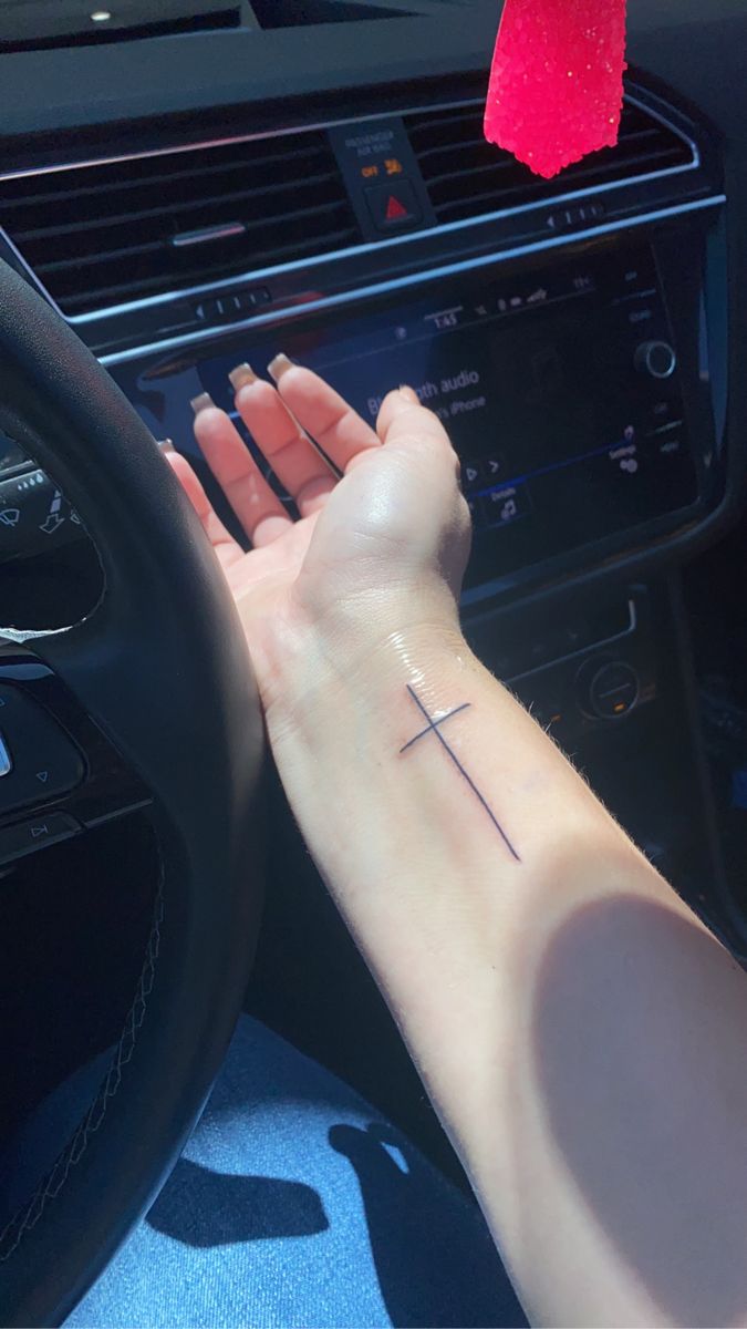 a woman's hand on the steering wheel of a car with a cross tattoo