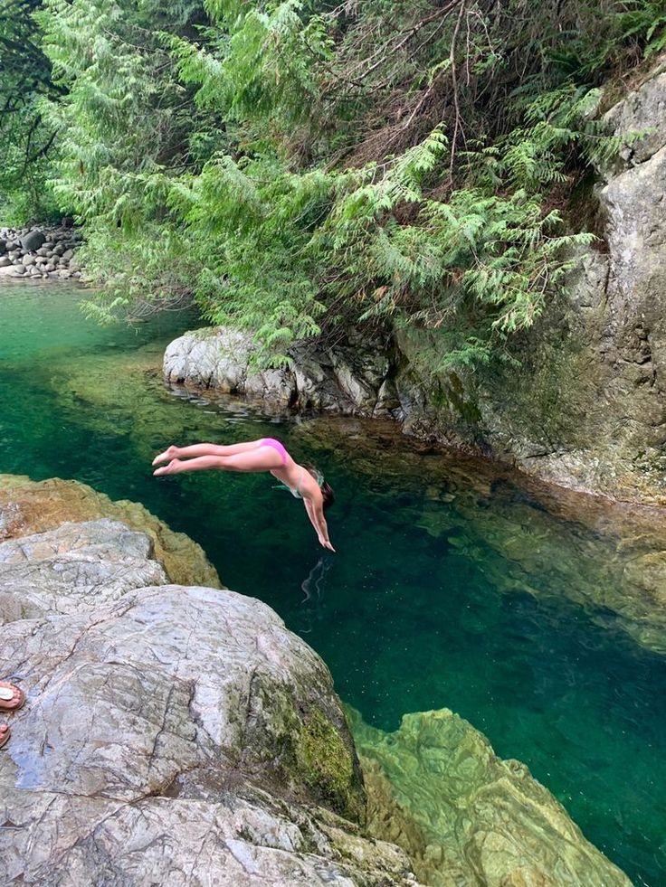 a person diving into the water from rocks in a river with green trees around them