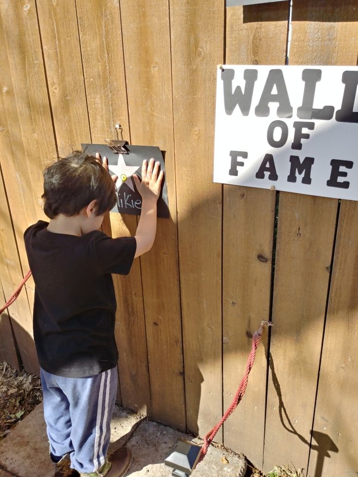 a little boy that is standing in front of a fence with a sign on it