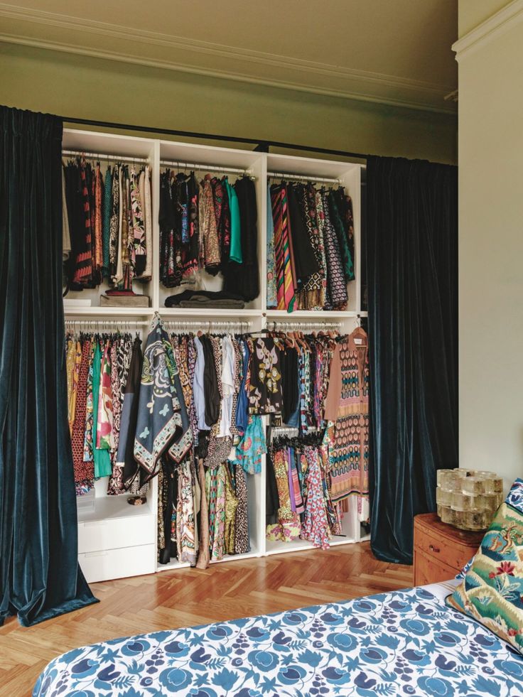 an organized closet with clothes and scarves hanging on the wall next to a bed