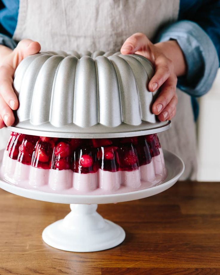 a person holding a cake on top of a white platter filled with strawberries