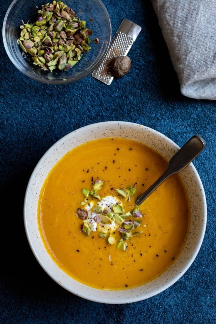 there is a bowl of soup on the table next to a plate with nuts and other food