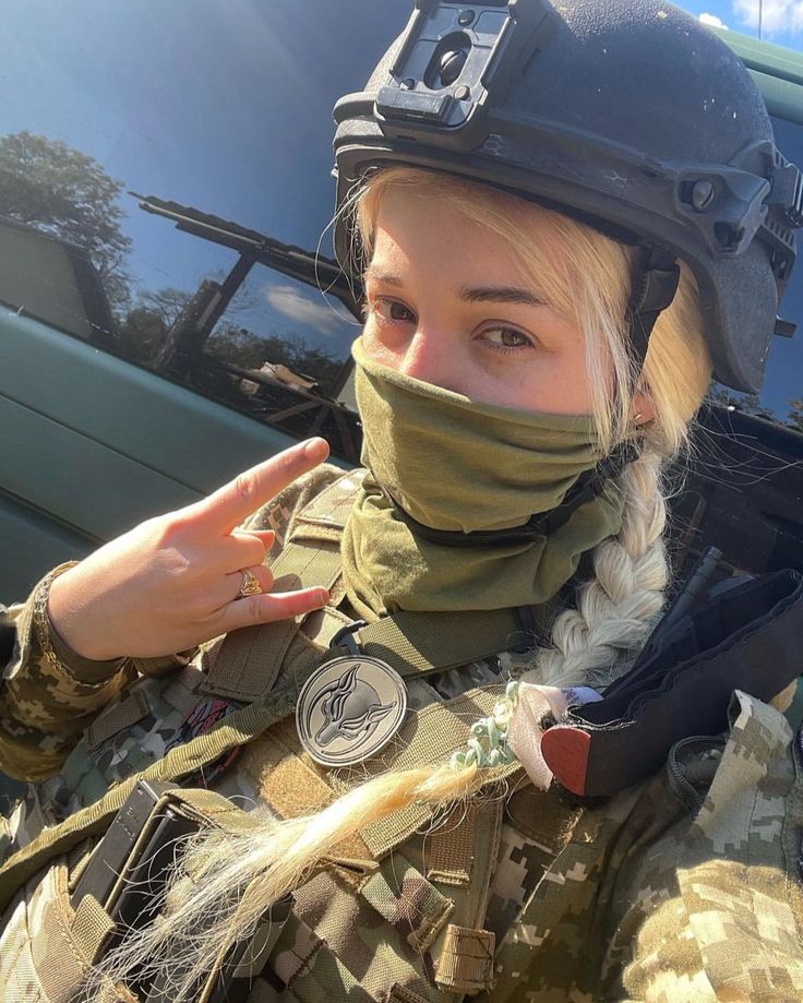 a woman wearing a helmet and scarf with her hand in the air while standing next to a vehicle