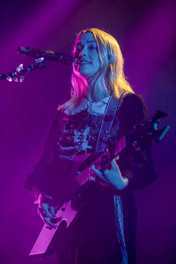 a woman holding a guitar while standing in front of a microphone and purple light behind her