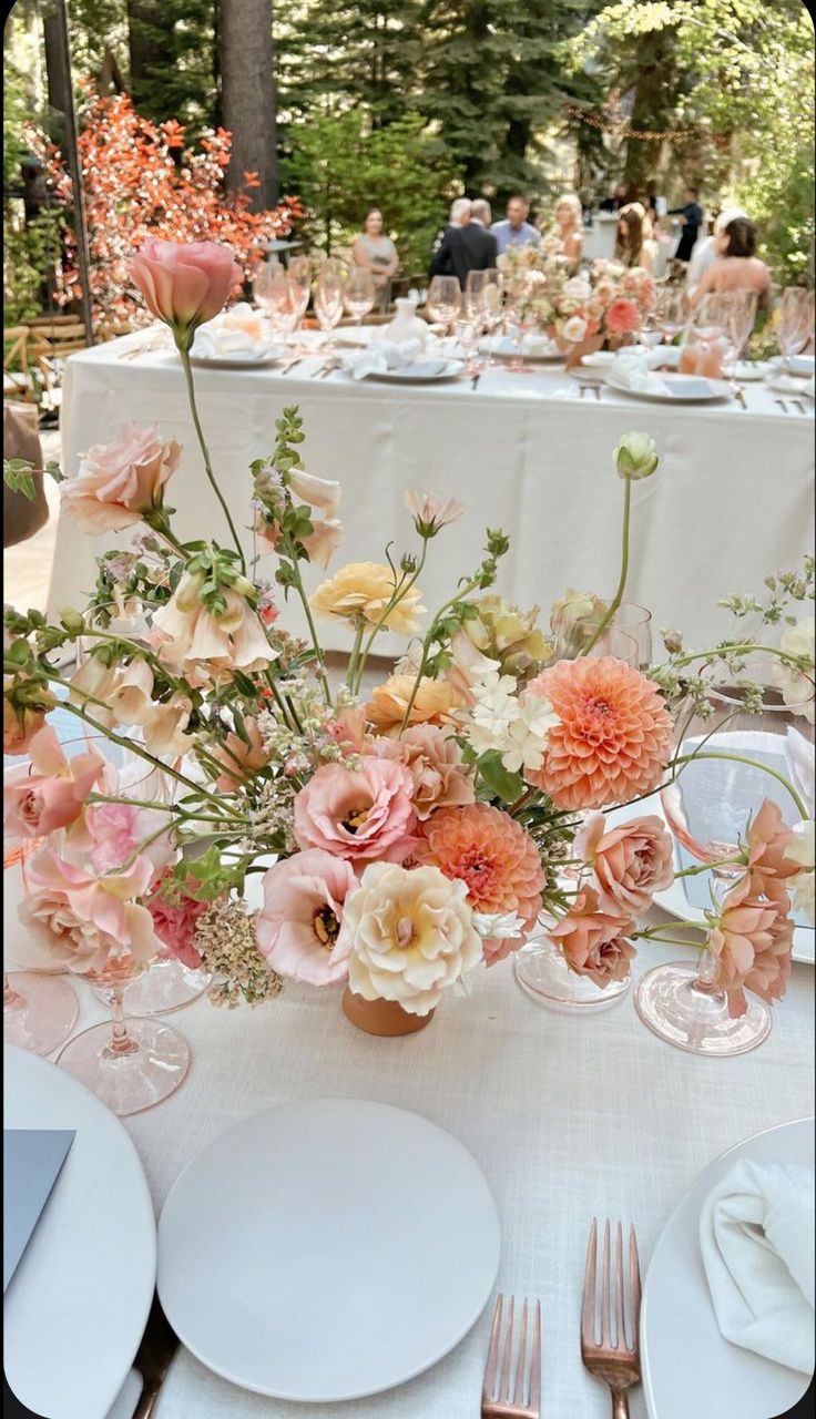 an arrangement of flowers in a vase on a table with white plates and silverware