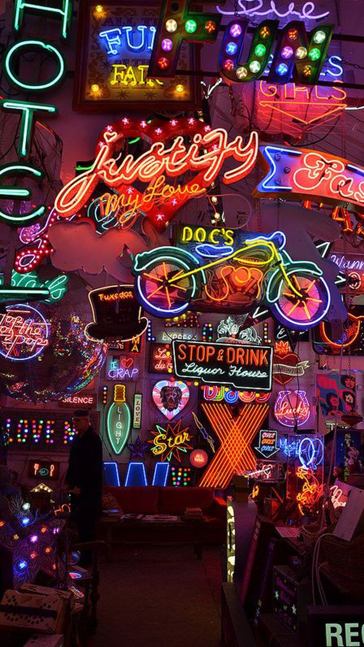 many neon signs are lit up on the wall in this shop's storefront