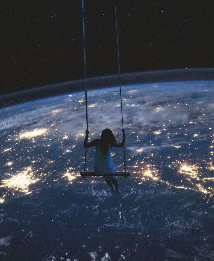 a girl on a swing suspended above the earth at night, with lights in the background